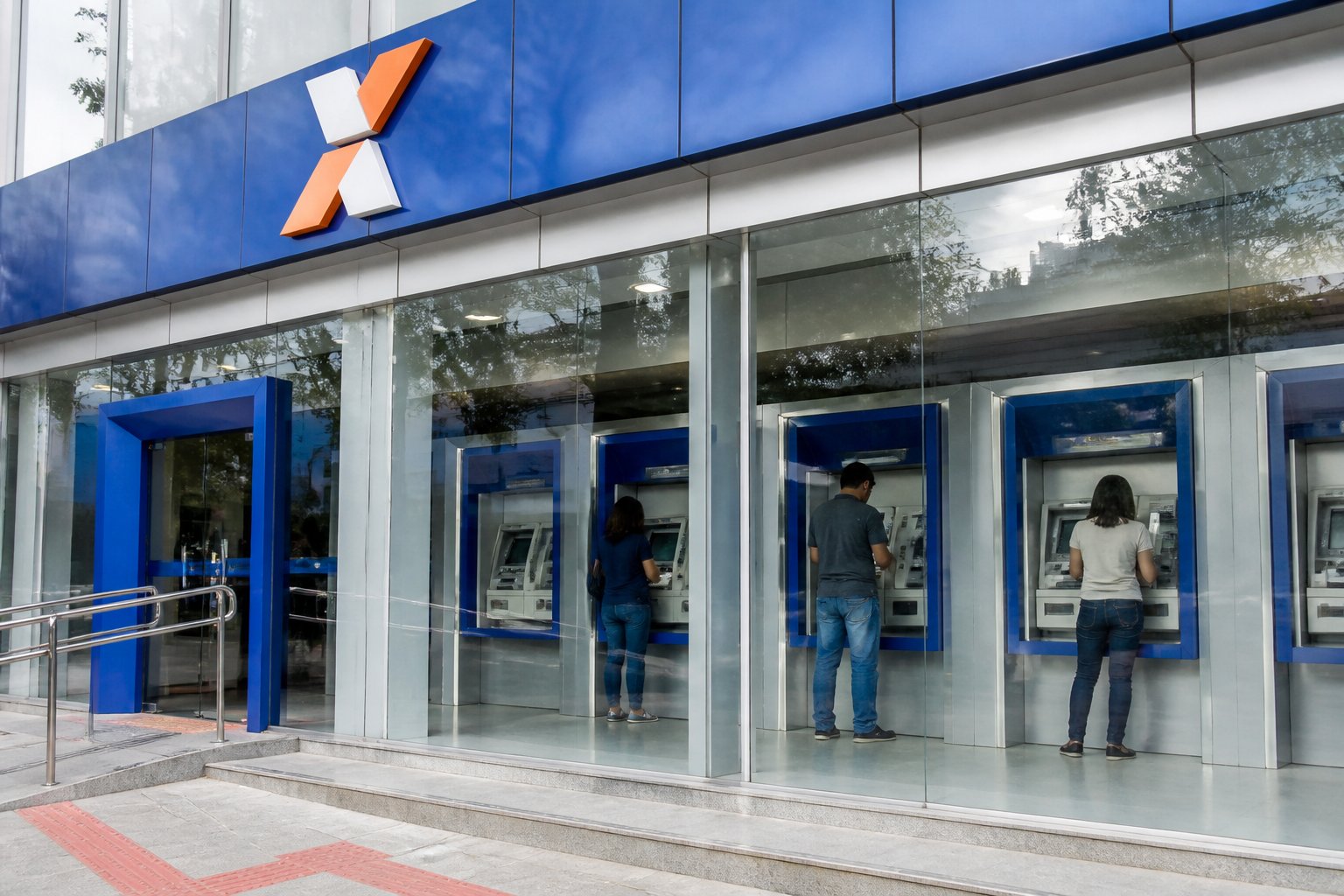 Fachada de uma agência da Caixa Econômica Federal com caixas eletrônicos visíveis e pessoas usando os terminais.